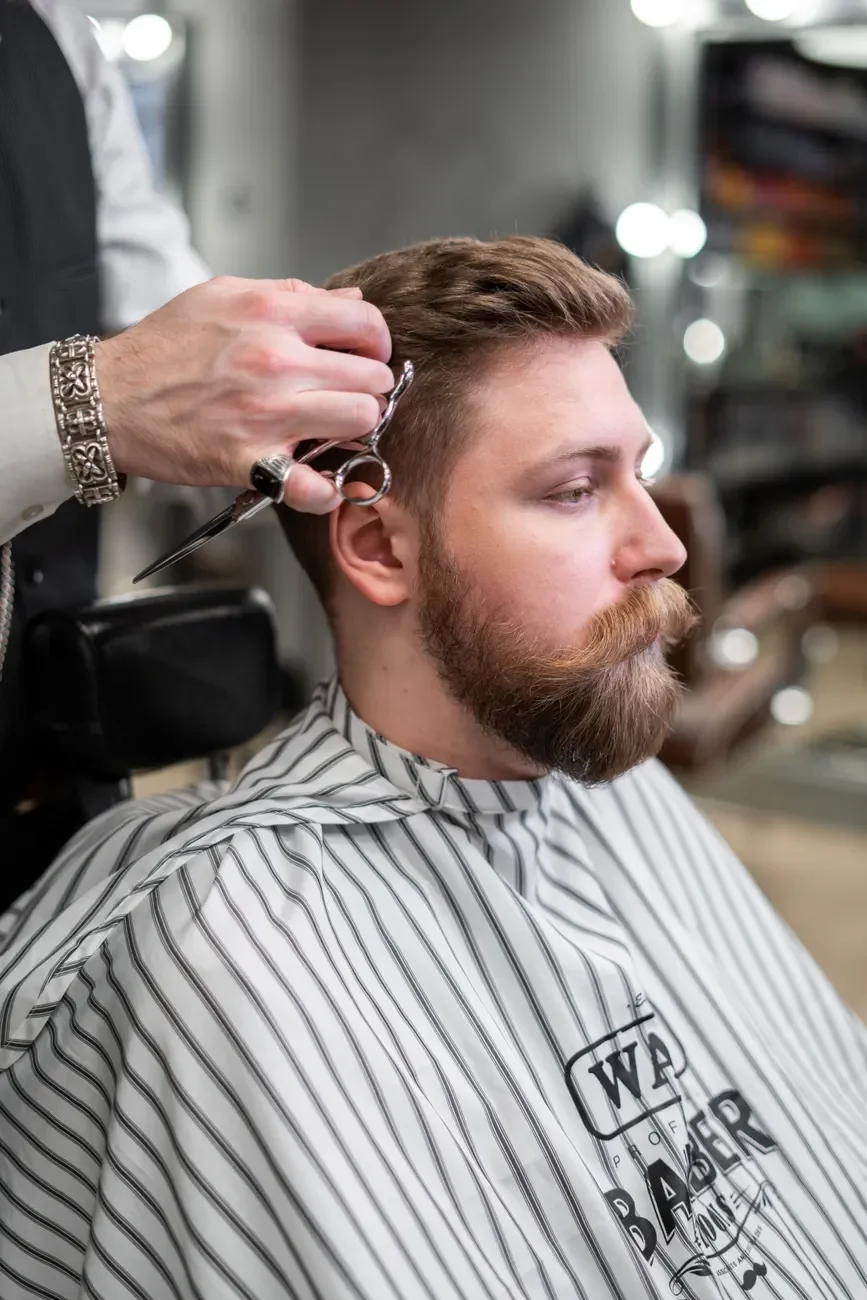 A barber trimming a bearded man's hair with scissors (stock photo)